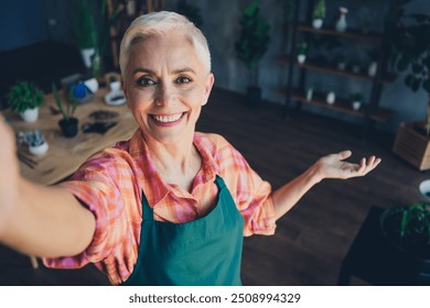 Photo portrait of lovely pensioner lady florist selfie photo hand point gesture wear apron working flower shop studio small business - Powered by Shutterstock