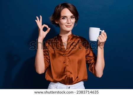 Photo portrait of lovely young lady hold coffee mug show okey symbol wear trendy brown blouse isolated on dark blue color background