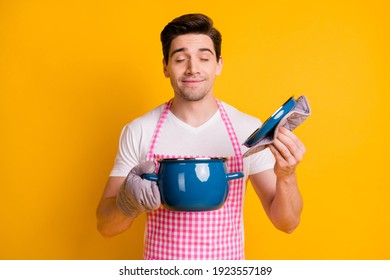 Photo portrait of man in kitchen gloves opening pot smelling food inside isolated on vivid yellow colored background
