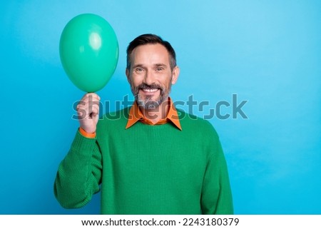 Photo portrait of mature attractive male hold air balloon toothy beaming smile wear trendy green outfit isolated on blue color background