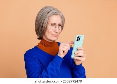 Photo portrait of nice senior woman hold device read news wear trendy blue outfit isolated on beige color background - Powered by Shutterstock