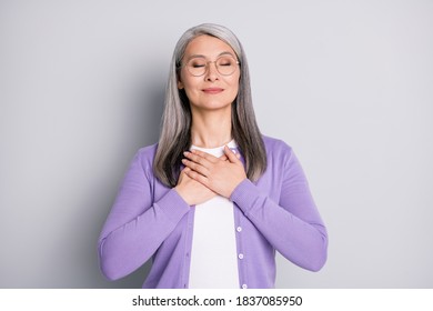 Photo Portrait Of Old Woman Holding Two Hands On Chest With Closed Eyes Dreaming Wearing Casual Violet Cardigan Isolated On Grey Colored Background