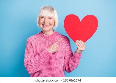 Photo portrait of old woman pointing finger at holding heart card in one hand isolated on pastel blue colored background