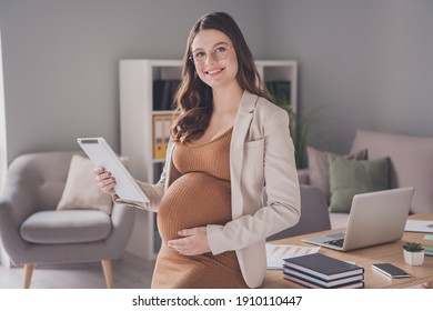 Photo portrait of pregnant lady with tablet touching belly sitting on desk in modern office - Powered by Shutterstock