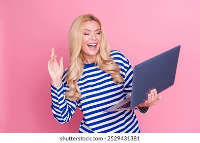 Photo portrait of pretty mature female hold netbook video call wave hand wear trendy striped outfit isolated on pink color background - Powered by Shutterstock