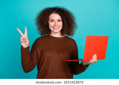 Photo portrait of pretty young girl hold netbook show v-sign wear trendy brown outfit isolated on cyan color background