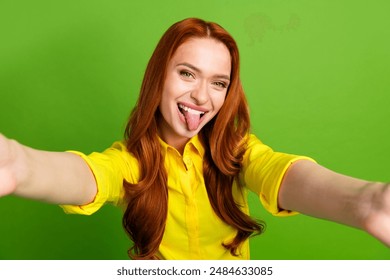 Photo portrait of pretty young girl take selfie photo stick tongue out wear trendy yellow outfit isolated on green color background