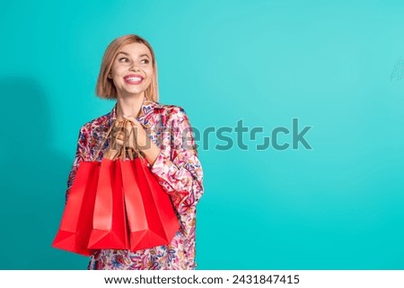 Photo portrait of pretty young girl hold shopping bags look empty space wear trendy pink print garment isolated on cyan color background
