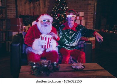 Photo portrait of santa claus and elf eating popcorn using remote watching movie on sofa in 3d glasses