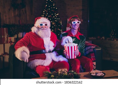 Photo portrait of santa claus and elf eating popcorn watching movie on sofa in 3d glasses