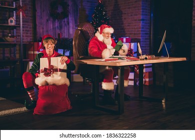 Photo Portrait Of Santa Claus Reading Green Letter From Child And Elf Putting Wrapped Present Into Sack