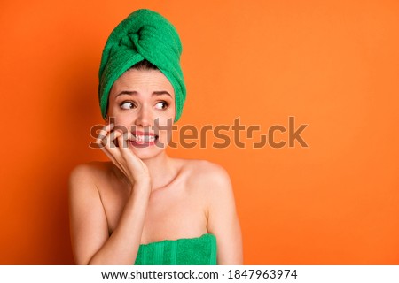 Photo portrait of scared woman biting fingers nails looking at blank space isolated on bright orange colored background