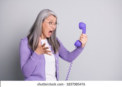 Photo portrait of senior mad furious stressed woman shouting screaming loudly keeping handset of retro violet phone with wire isolated on grey color background
