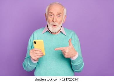 Photo portrait of senior man showing cellphone surprised advising in teal clothes isolated on pastel purple color background