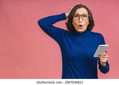 Photo Portrait Of Shocked Amazed Surprised Senior Aged Mature Woman Holding Mobile Phone Seeing Crazy Discounts Wearing Casual Isolated On Pink Background.