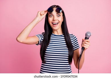 Photo Portrait Of Shocked Woman Lifting Up Glasses Holding Microphone In One Hand Isolated On Pastel Pink Colored Background