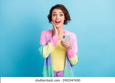 Photo Portrait Of Shocked Woman With Open Mouth Touching Face Cheek With One Hand Holding Phone Isolated On Pastel Blue Colored Background