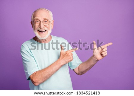 Photo portrait of smiling old man pointing two fingers to side isolated on vivid violet colored background