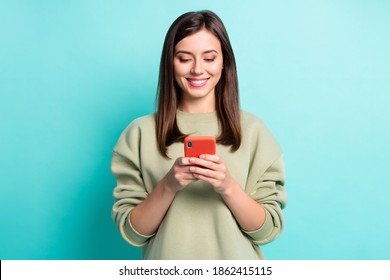 Photo portrait of smiling woman typing holding phone in two hands isolated on vivid turquoise colored background