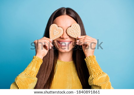Photo portrait of woman covering two eyes with heart-shaped gingerbread cookies isolated on pastel blue colored background