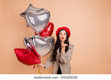 Photo portrait of woman with helium balloons sending air kiss isolated on pastel beige colored background