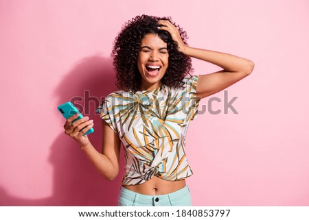 Photo portrait of woman holding head with one hand laughing holding phone isolated on pastel pink colored background