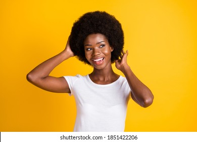Photo portrait of young african american woman touching afro hairstyle with two hands smiling wearing white t-shirt isolated on vivid yellow colored background