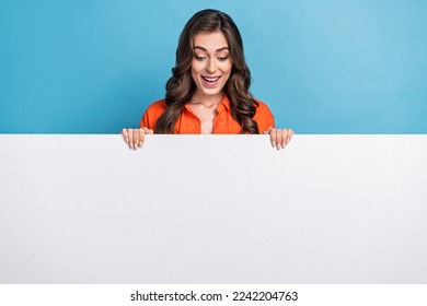 Photo portrait of young attractive woman looking down white billboard poster wear trendy orange garment isolated on blue color background