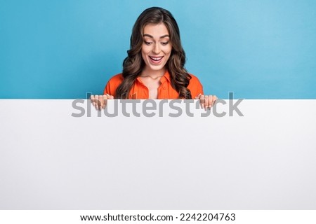Photo portrait of young attractive woman looking down white billboard poster wear trendy orange garment isolated on blue color background