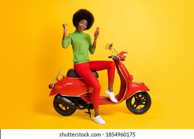 Photo portrait of young brunette african american biker on red bike holding cellphone receiving winning sms message wearing casual outfit isolated on vivid yellow colored background