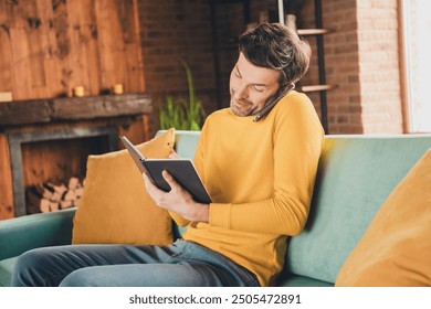 Photo portrait of young guy sit couch write notebook talk phone dressed yellow garment spend pastime spacious house indoors room