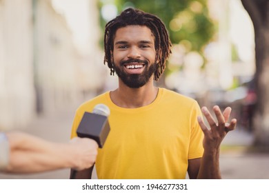 Photo portrait of young man smiling giving interview to journalist talking in microphone on street
