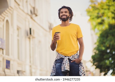 Photo portrait of young man wearing stylish outfit dreadlocks drinking coffee while walking on city streets with green trees - Powered by Shutterstock