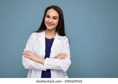 Photo portrait of young pretty beautiful positive smiling brunette woman with sincere emotions wearing white medical coat isolated over blue background with copy space and holding crossed arms