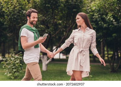 Photo portriat young couple smiling walking in green park holding hands guy using smartphone looking on map - Powered by Shutterstock