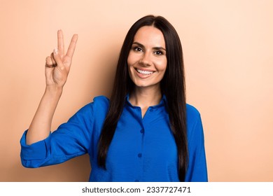 Photo of positive adorable girl wear blue clothes hand showing v-sign symbol good mood isolated on beige color background