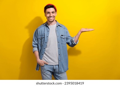 Photo of positive charming guy wear denim jacket holding arm empty space isolated yellow color background - Powered by Shutterstock