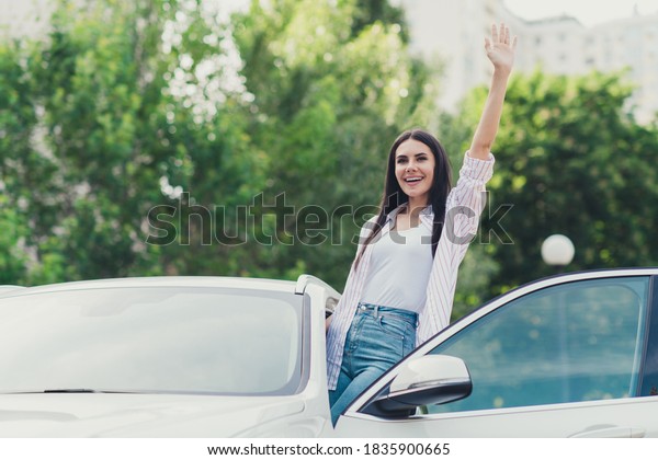 Photo of positive cheerful girl ride drive\
automobile see her friends, walking town street open door wave hand\
invite summer weekend\
outside