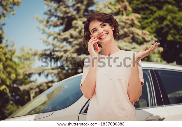 Photo of positive cheerful girl ride drive\
automobile call friend smartphone arrange summer vacation meeting\
in town center outdoors