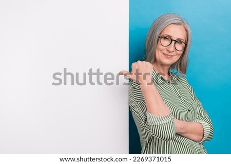 Photo of positive cheerful senior lady clerk dressed striped shirt pointing thumb back empty space isolated blue color background