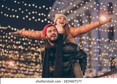 Photo of positive couple having fun christmas x-mas around evening outside illumination boyfriend piggyback girlfriend holding hands fly - Powered by Shutterstock
