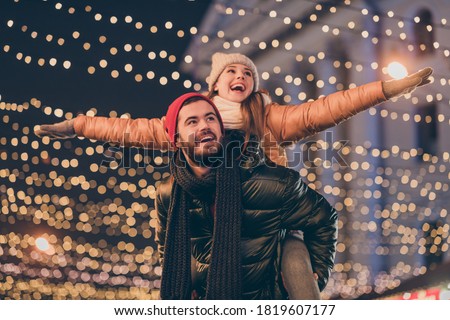 Photo of positive couple having fun christmas x-mas around evening outside illumination boyfriend piggyback girlfriend holding hands fly