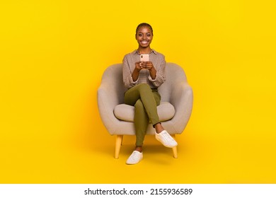Photo of positive cute lady dressed checkered shirt sitting chair chatting modern gadget isolated yellow color background