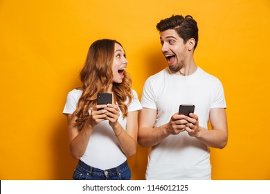 Photo of positive excited people man and woman screaming and looking at each other while both using mobile phones isolated over yellow background - Shutterstock ID 1146012125
