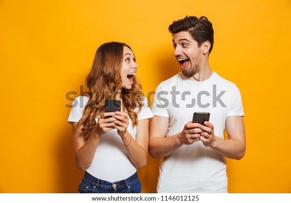 Photo of positive excited people man and woman
screaming and looking at each other while both using mobile phones
isolated over yellow
background