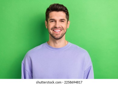 Photo of positive funny young guy dressed violet clothes smiling showing white teeth isolated green color background