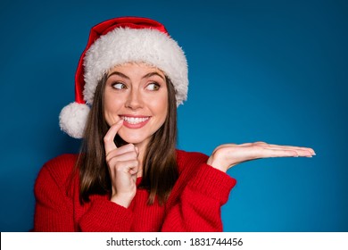 Photo positive girl in santa claus hat hold hand demonstrate x-mas newyear advert promo touch finger teeth wear warm winter season clothes isolated blue gradient color background