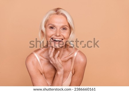 Photo of positive lovely retired lady toothy smile dressed stylish bra enjoying ideal skin serum cream isolated on beige color background 商業照片 © 