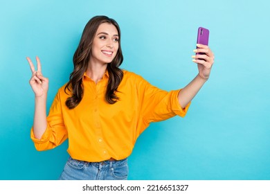 Photo of positive nice girl hold telephone make selfie demonstrate v-sign isolated on blue color background