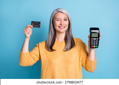 Photo Of Positive Old Woman Hold Credit Card Machine Reader Recommend Bank Purchase Wink Blink Wear Style Stylish Trendy Sweater Isolated Over Blue Color Background